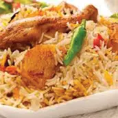 A plate of Chicken Biryani garnished with fresh cilantro and fried onions, served with a side of raita and lemon wedges.