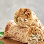 A rolled Chicken Shawarma wrap filled with sliced grilled chicken, lettuce, tomatoes, and garlic sauce, served with pickles and fries on the side.