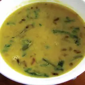 A bowl of Masoor Dal, red lentils cooked in a mildly spiced Indian curry, topped with a tempering of mustard seeds, garlic, and red chili, and garnished with fresh cilantro.